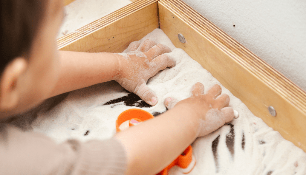 Preschooler engaged in independent play activities with a sensory bin filled with colorful textures and toys.