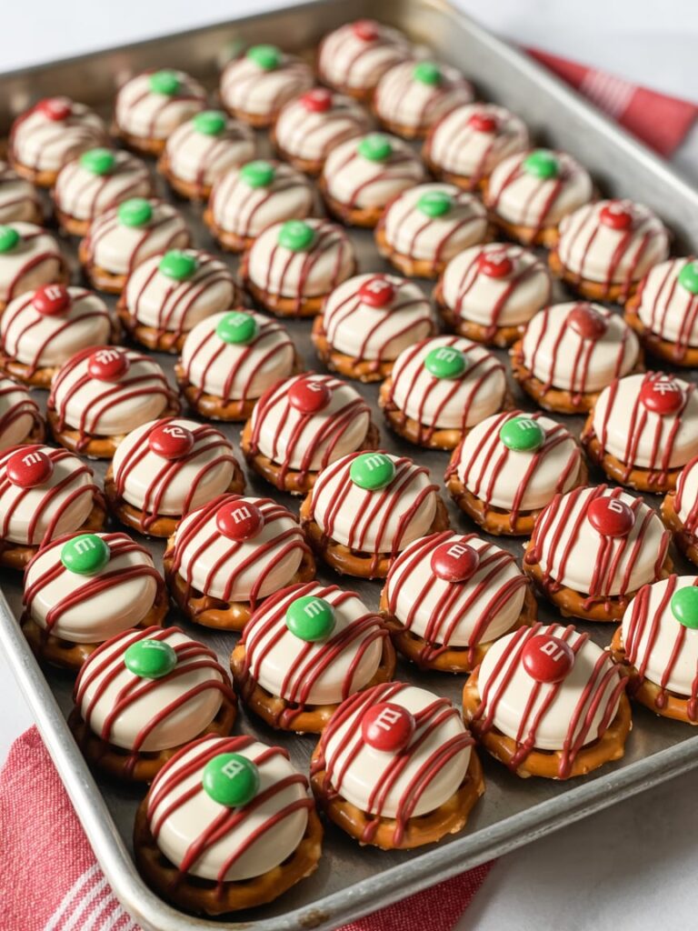 Tray of peppermint pretzel bites made with pretzels, melted white chocolate, red drizzle, and red and green M&M candies arranged neatly for holiday gifting.