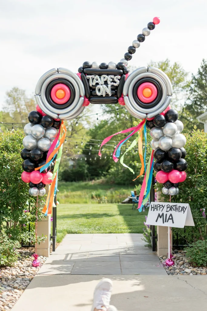 Boombox-shaped balloon arch entrance in black, gold, and neon orange for a 90's birthday party