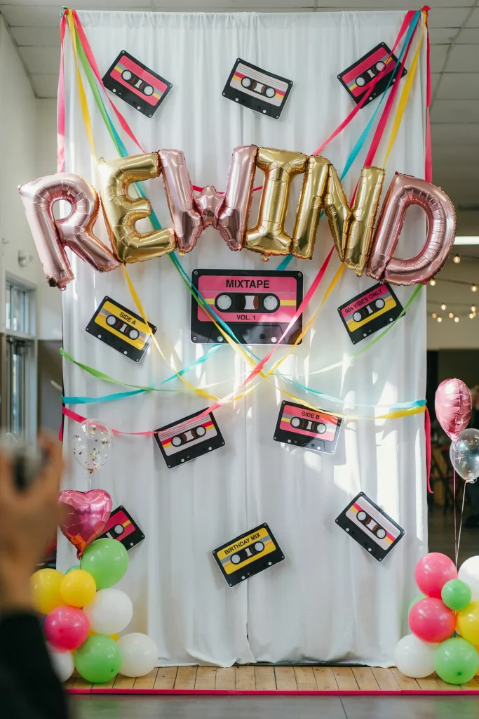 Neon cassette tape photo backdrop with pink and yellow balloon garland for a 90's kids party
