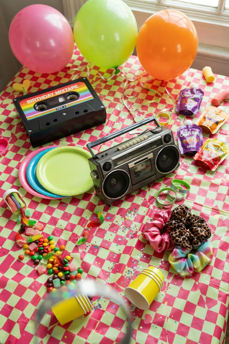 A neon-lit party table with a cassette tape backdrop, rainbow snacks, and slap bracelets scattered across the tablecloth, shot from above in bright, saturated color