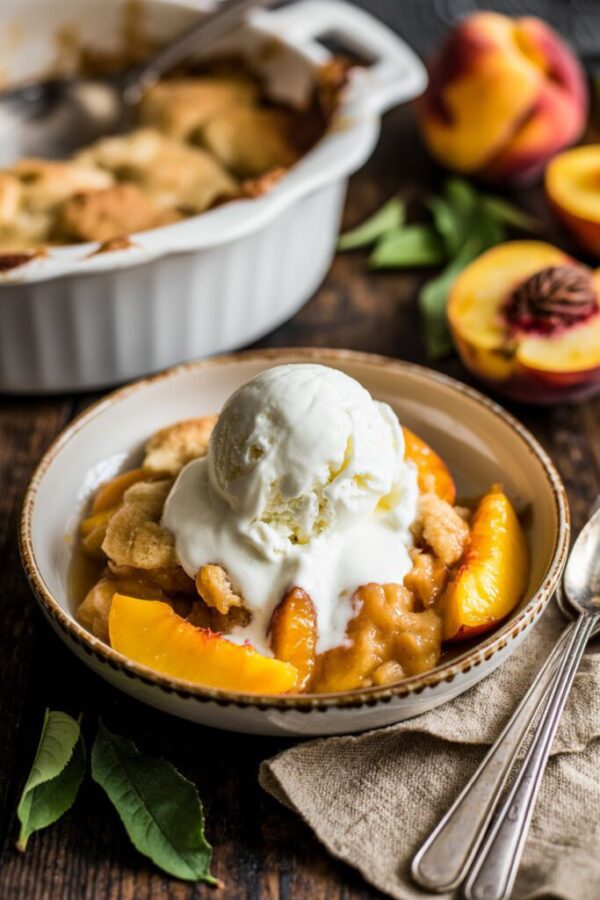 Crockpot peach cobbler with golden biscuit topping and visible peach syrup served in a rustic setting.
