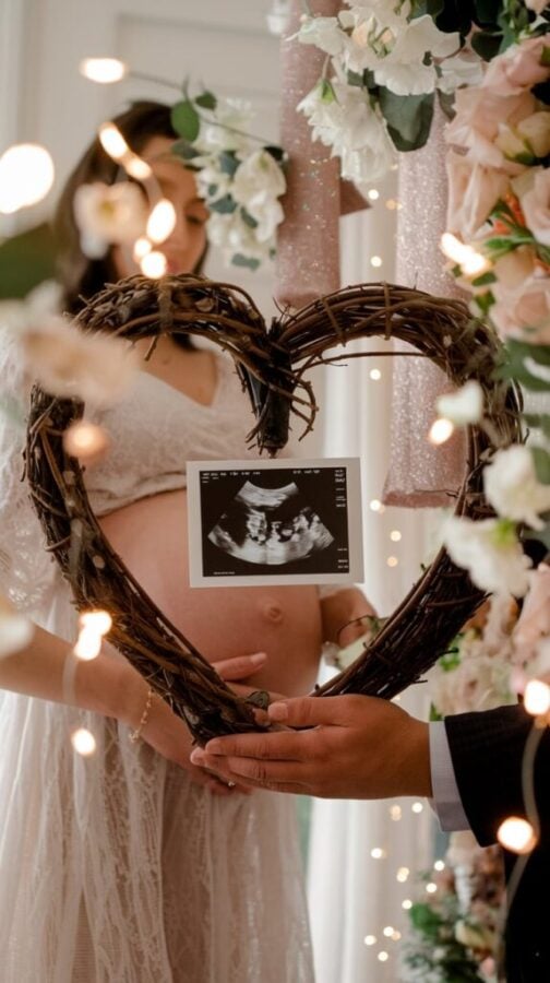 Mom posing with a heart-shaped wreath frame surrounding her baby bump, decorated with flowers and glitter