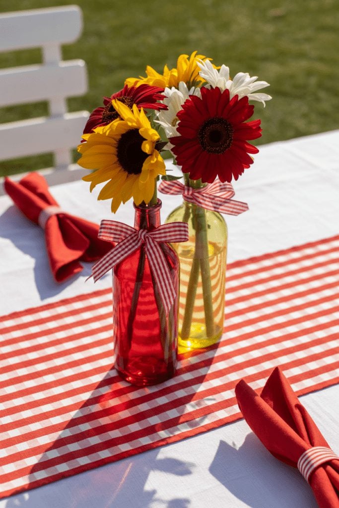 Bright wildflowers in small glass bottles with a red gingham table runner