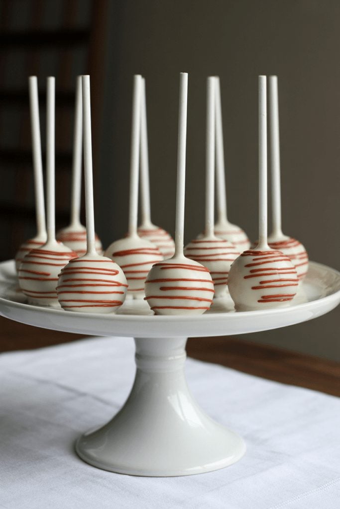White cake pops with a soft red drizzle displayed on a cake stand