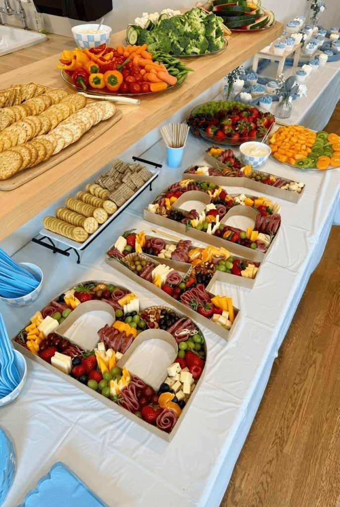 Grazing table with charcuterie boxes, fresh vegetables, and fruit platters for a BBQ baby shower