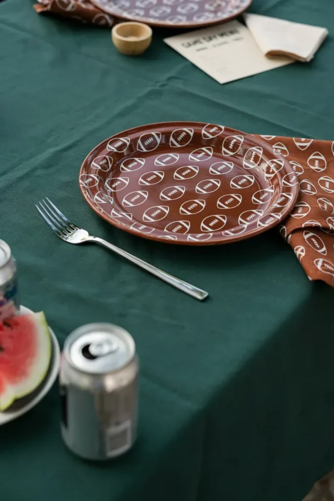 A place setting with brown football-print plates, napkins, and forks arranged on a green tablecloth.