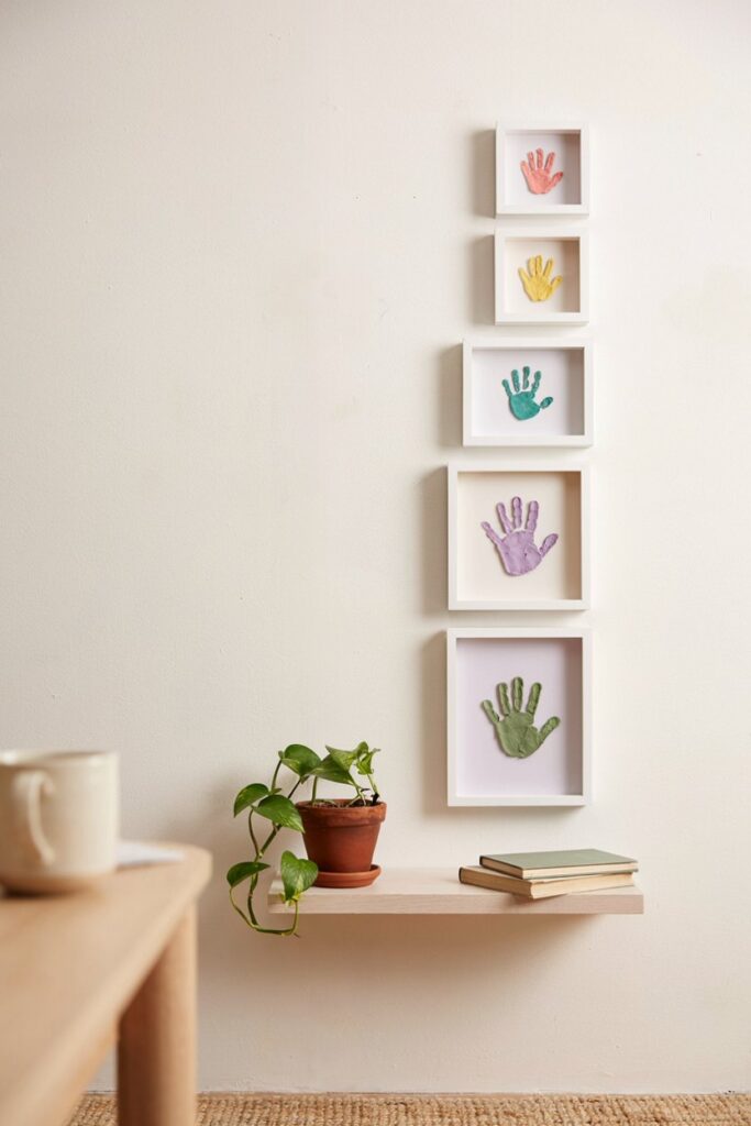 Row of small clay discs with handprints of increasing size displayed on a wooden shelf