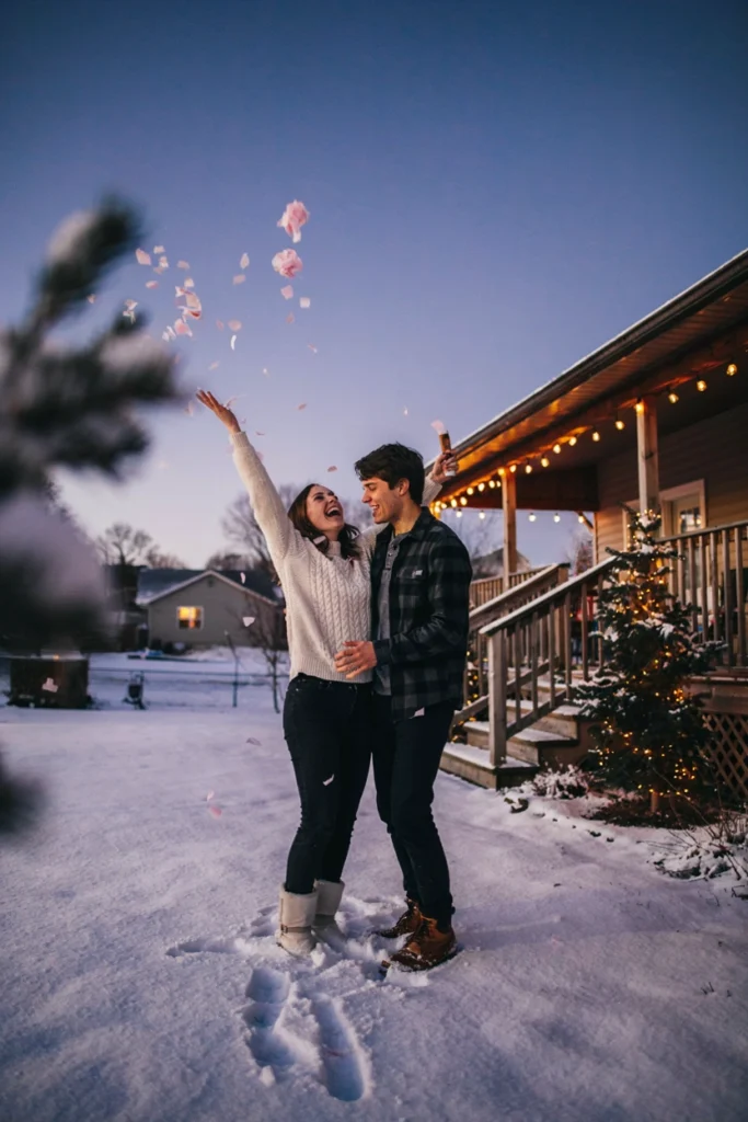 Couple outside in the snow with a pink confetti cannon burst and string lights behind them