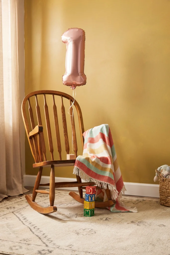 Baby sitting in the same wooden rocking chair by a window for an annual milestone birthday photo