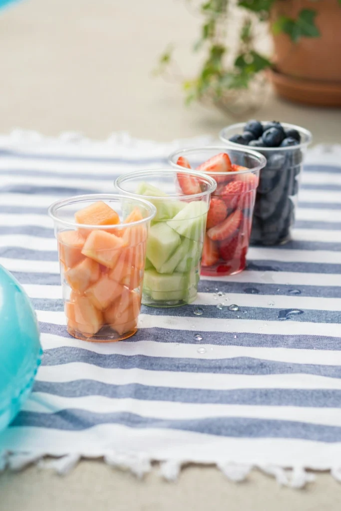 Individual clear plastic cups filled with diced cantaloupe, honeydew, and strawberries