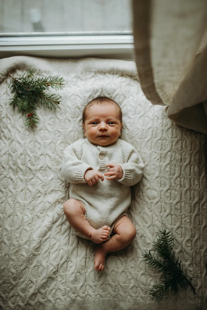 Newborn baby lying on cream milestone blanket for first Christmas photo