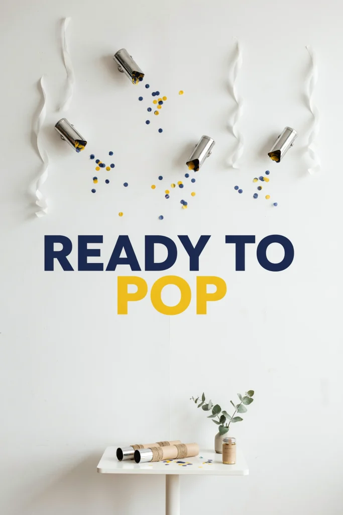 A feature wall decorated with geometric confetti cannons, navy blue and yellow circular paper confetti scattered artfully, white streamers, and "Ready to Pop" signage in bold lettering. Clean, minimalist aesthetic. Contemporary baby shower vibe.