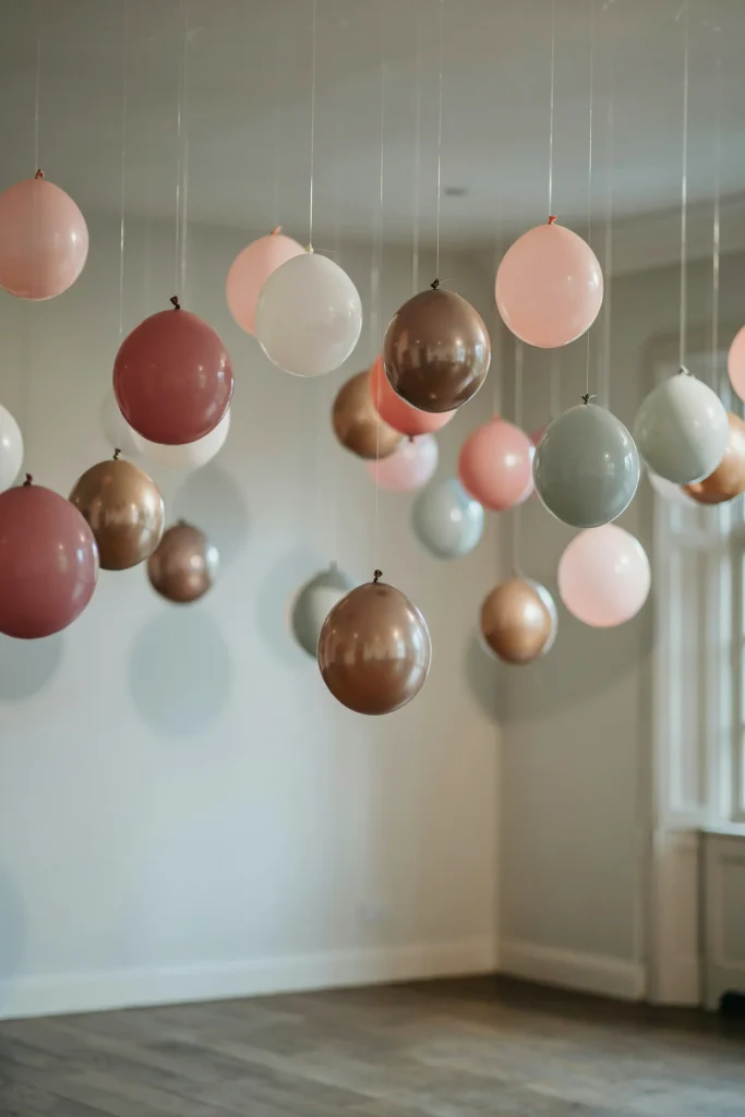 Individual balloons in coordinating colors tied to fishing line and dangling from the ceiling at varying heights. Creates a dreamy, whimsical overhead effect. Photos of the space show depth and celebration. Simple but impactful.