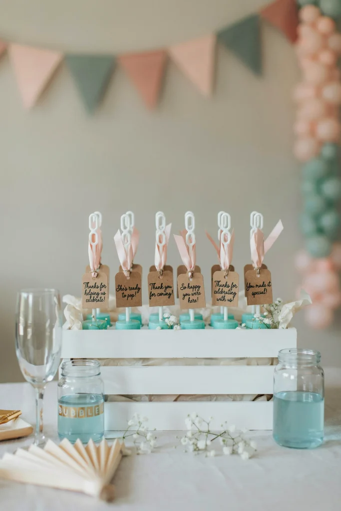 A table display of bubble wands tied with ribbon, each tagged with a custom "Thank You" label reading something like "Thanks for Helping Us Celebrate" or "She's Ready to Pop." Coordinated with the shower's color palette. Guests can grab on their way out.