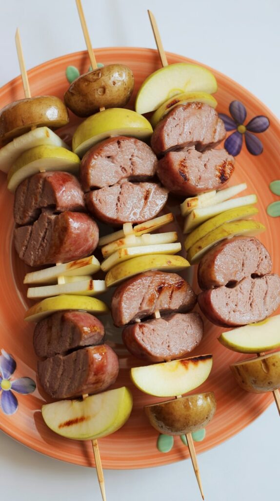 Grilled sausage and apple skewers with golden baby potatoes, arranged on an orange floral plate — a hearty fall-inspired appetizer or dinner idea perfect for entertaining.