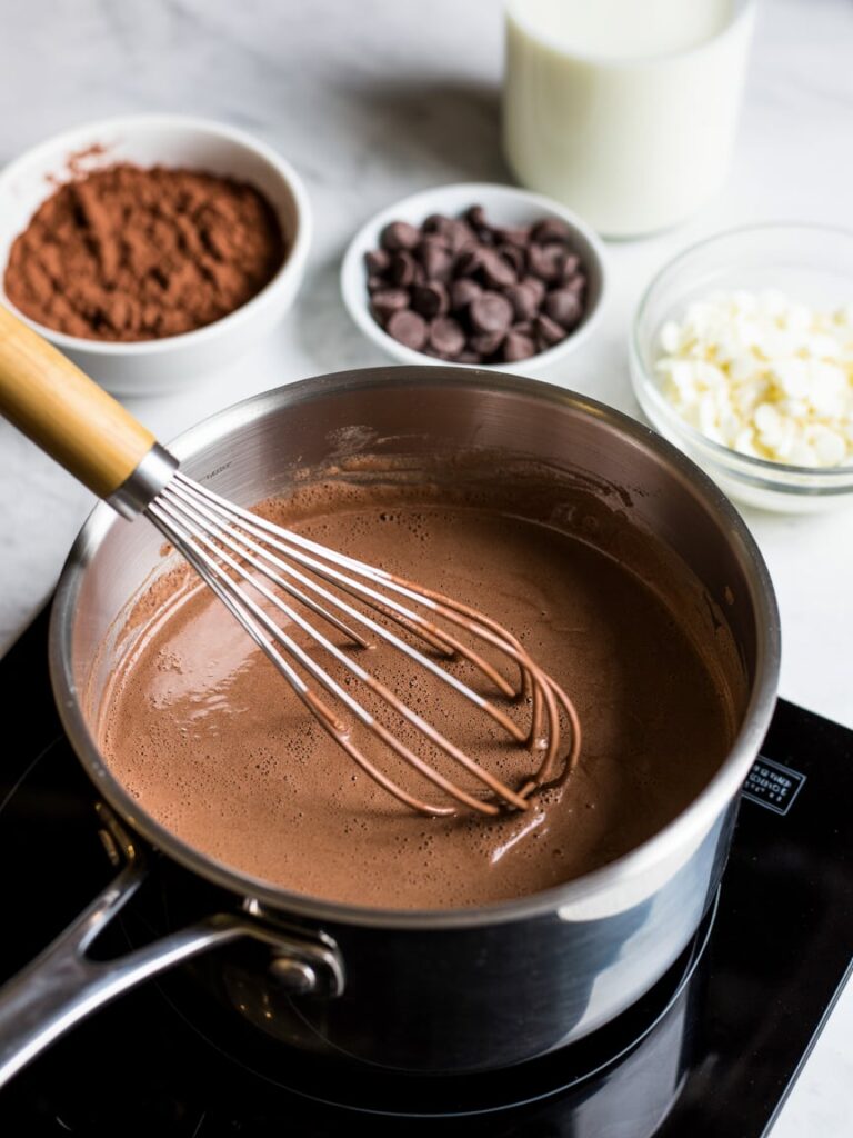 Cocoa mixture being whisked in a saucepan with chocolate ingredients beside it.
