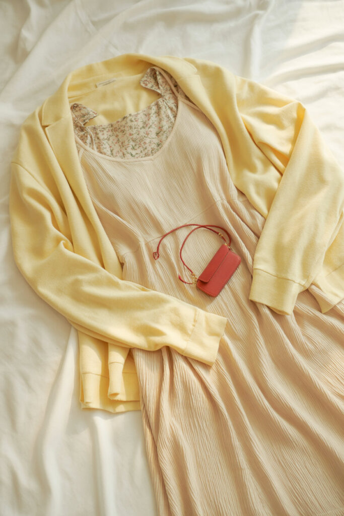 inspiration flat-lay including a neutral dress, pale yellow cardigan, soft floral prints, and a small red accessory captured in warm, clean lighting.