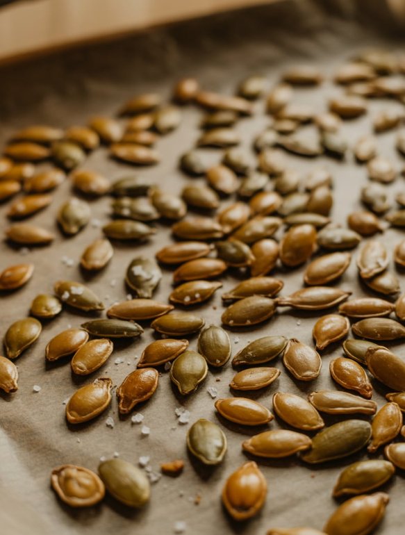 Close-up of roasted pumpkin seeds sprinkled with sea salt on a baking sheet — a simple, crunchy, and nutritious fall snack.