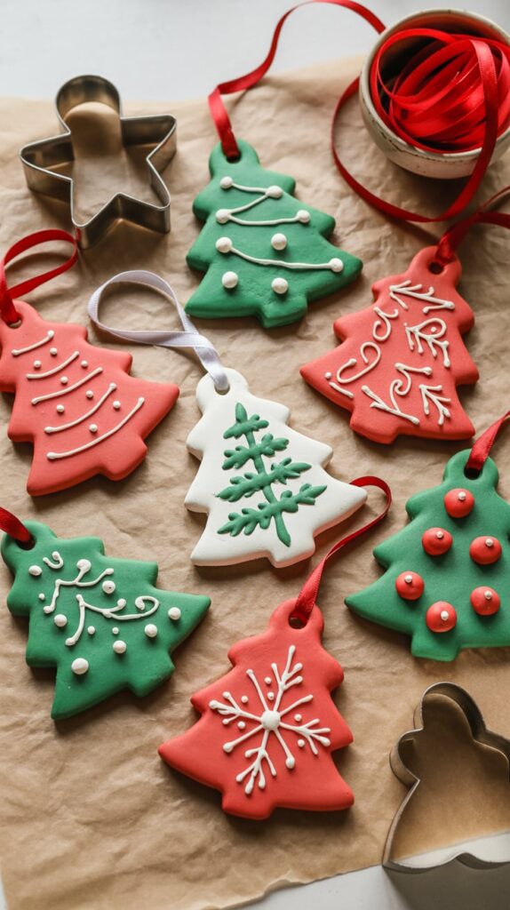 Handmade salt dough Christmas ornaments decorated with paint and ribbon on parchment paper beside cookie cutters.