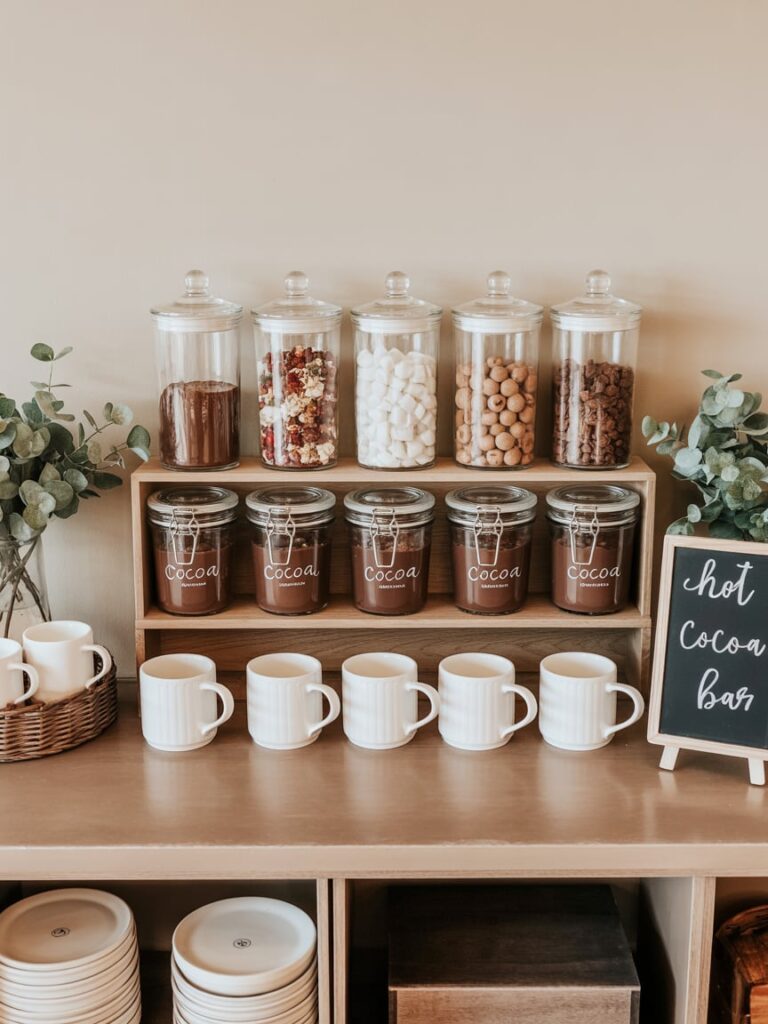Self-serve hot cocoa bar with mugs, jars of toppings, and simple winter décor.