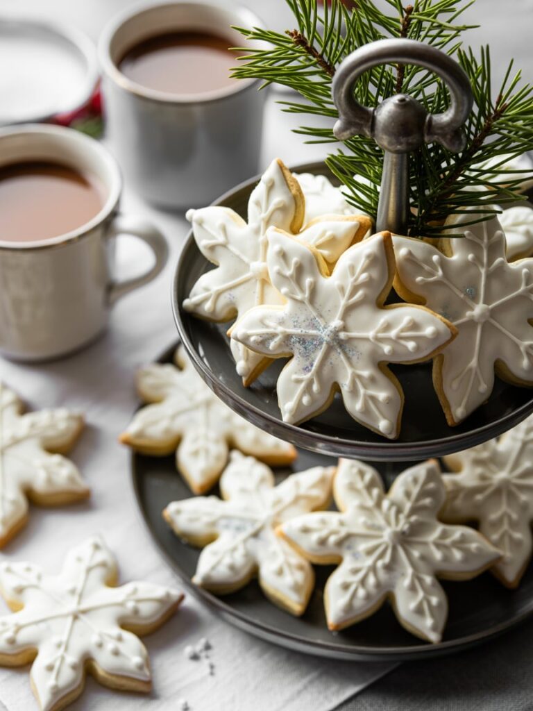 Snowflake sugar cookies with edible glitter served beside cocoa mugs for a winter baby shower.