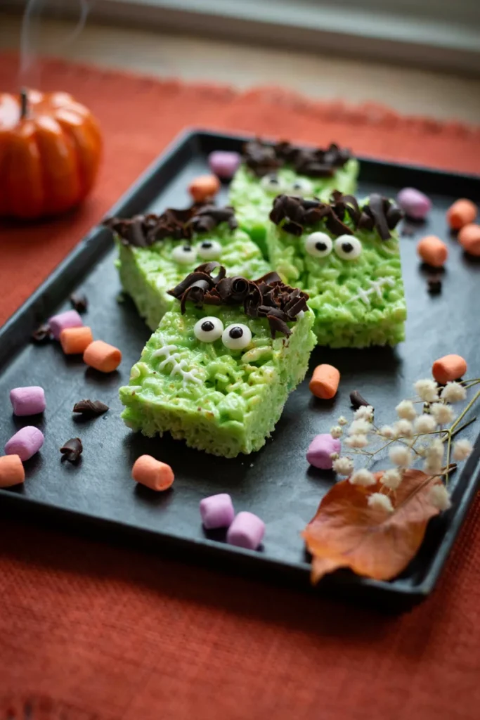 Green Rice Krispie treats decorated with chocolate hair and candy eyes to look like Frankenstein's monster