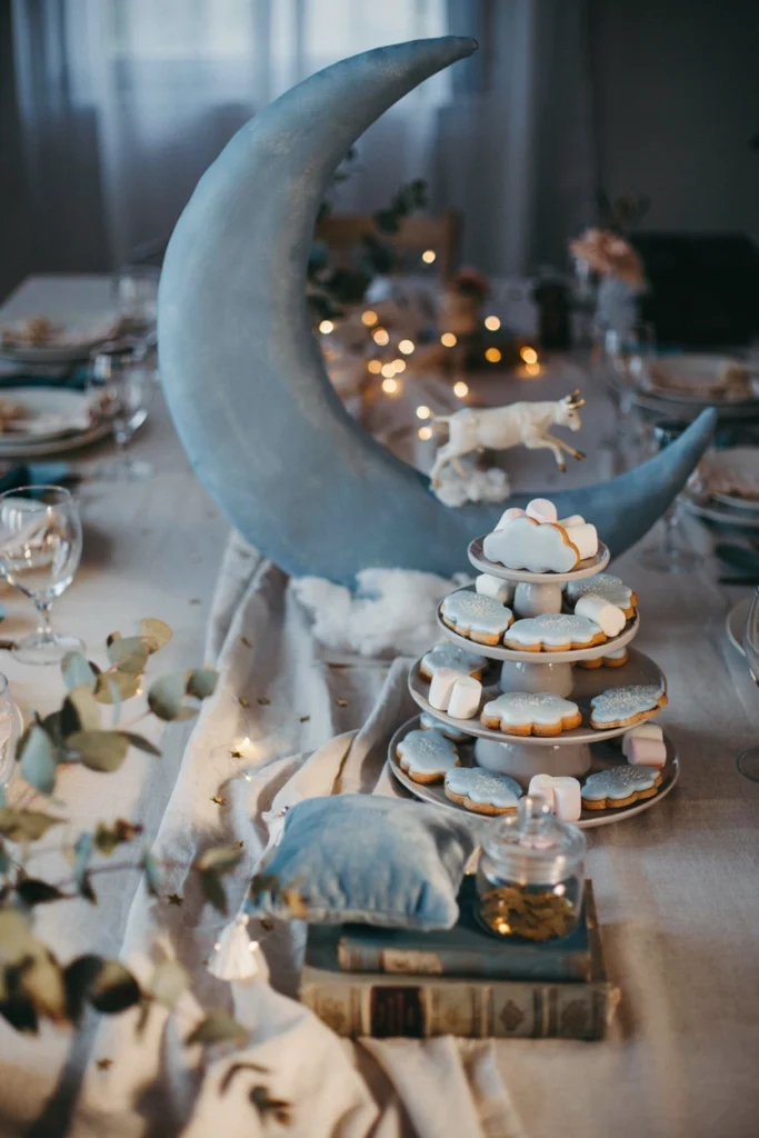Goodnight Moon baby shower tablescape in dusty blue and cream with a crescent moon backdrop and star-shaped confetti