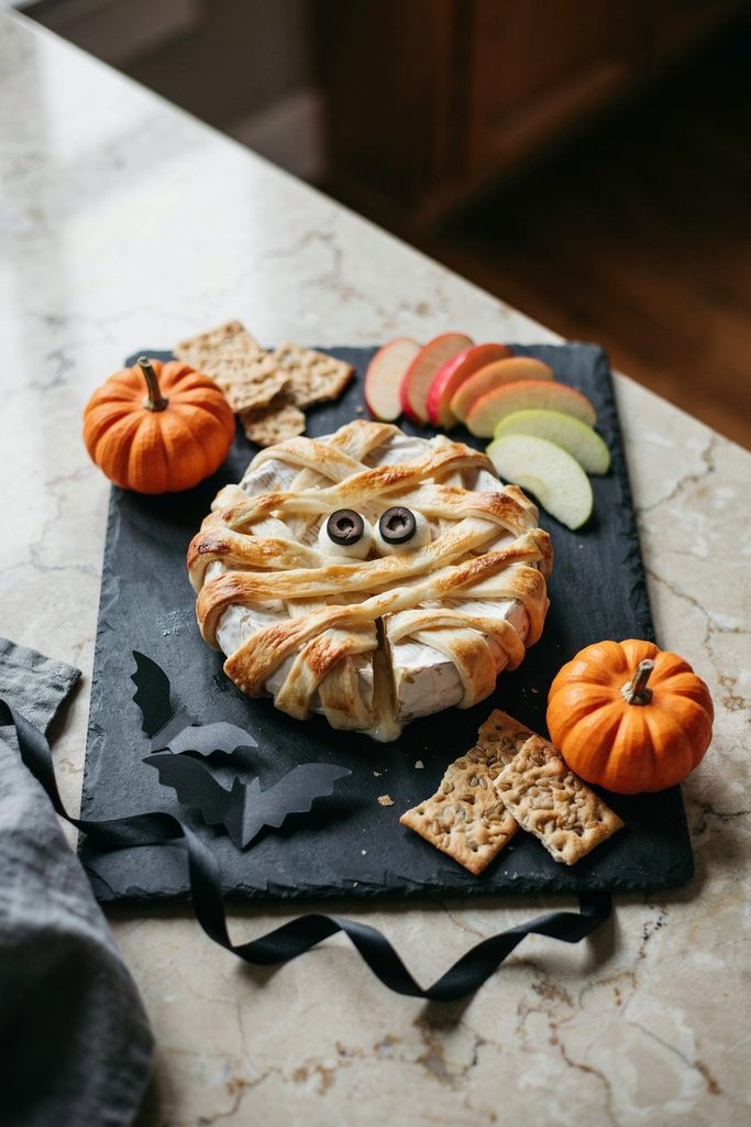 Halloween mummy baked brie wrapped in crescent dough strips with mozzarella pearl cheese eyeballs, apple slices and crackers, easy Halloween appetizer board