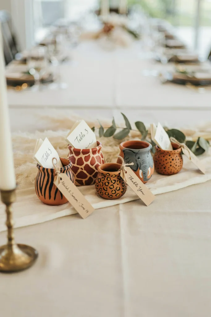 Small terra cotta pots painted with animal prints, stripes, or safari patterns, used to hold place cards, favor tags, or gift cards.