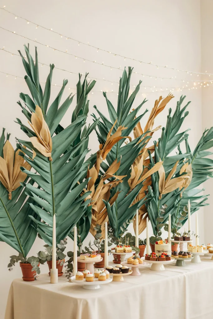Hand-made oversized palm fronds crafted from tissue paper or crepe paper in green and gold, positioned behind the cake table or backdrop