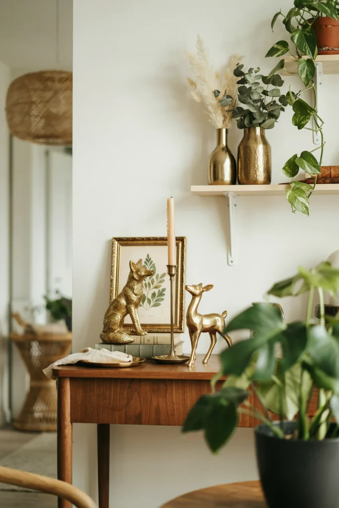 Candlestick holders, frames, animal figurines, and vases in gold and brass tones arranged on tables and shelves among the greenery and décor.