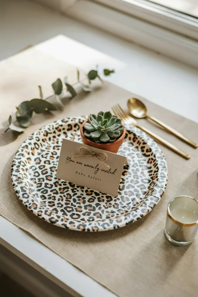 Close-up of a place setting with animal print paper plates, gold flatware, kraft paper placemat, small succulent pot as a favor, and a simple kraft card.