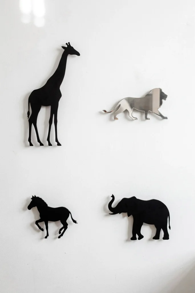 Plain white wall with large printed animal silhouette cutouts (giraffe, lion, zebra, elephant) in black matte or metallic finish, spaced asymmetrically.