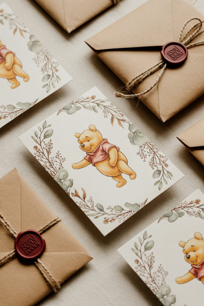 Flatlay of Pooh-inspired baby shower invitations with kraft envelopes, wax seal, twine, and soft botanical details.