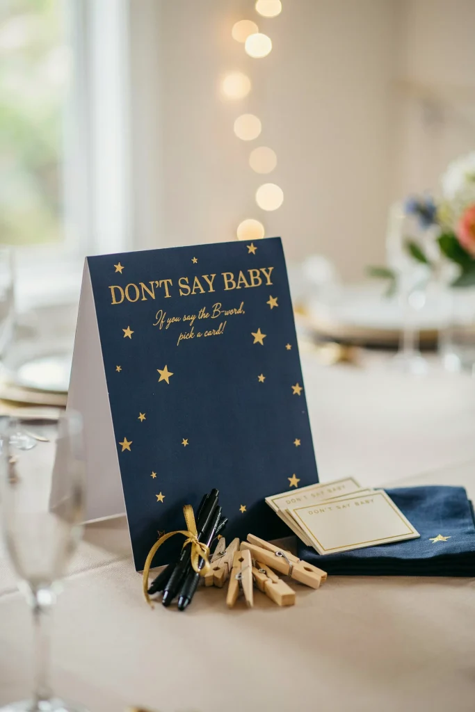 A small styled corner of the party with a "Don't Say Baby" game card display, navy and gold star-print signage, and a little stack of pens and clothespins.