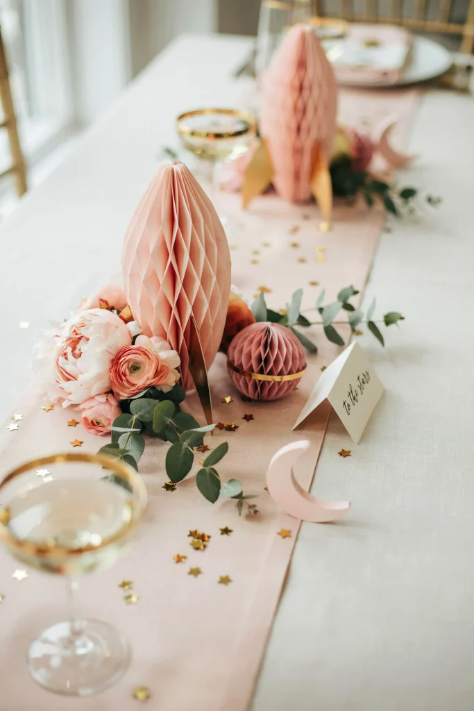 A table styled with pink, blush, and gold honeycomb rockets, planets, and stars, softer and more romantic than the bold navy version, with pink florals tucked alongside.