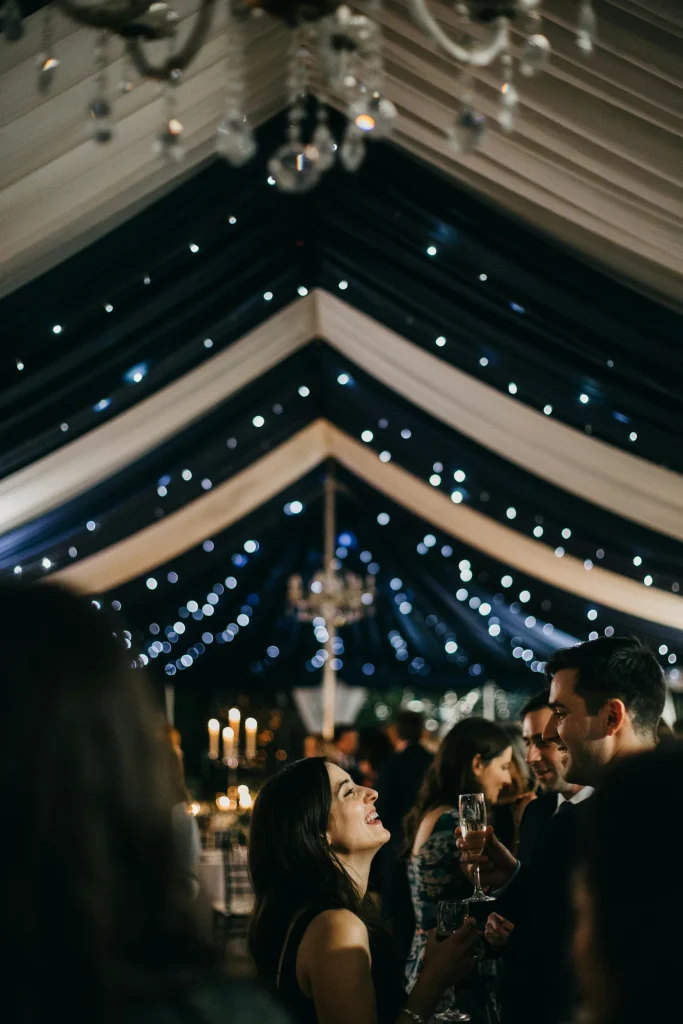 The underside of a white event tent draped with navy fabric and twinkle lights to mimic a starry sky, viewed from below as guests mingle beneath it.