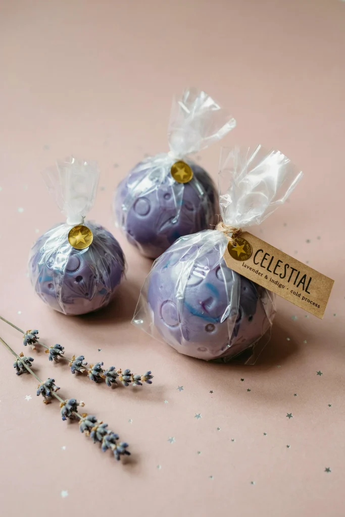 Small swirled purple-and-blue handmade soap bars shaped like planets, wrapped in clear cellophane with a star sticker seal.