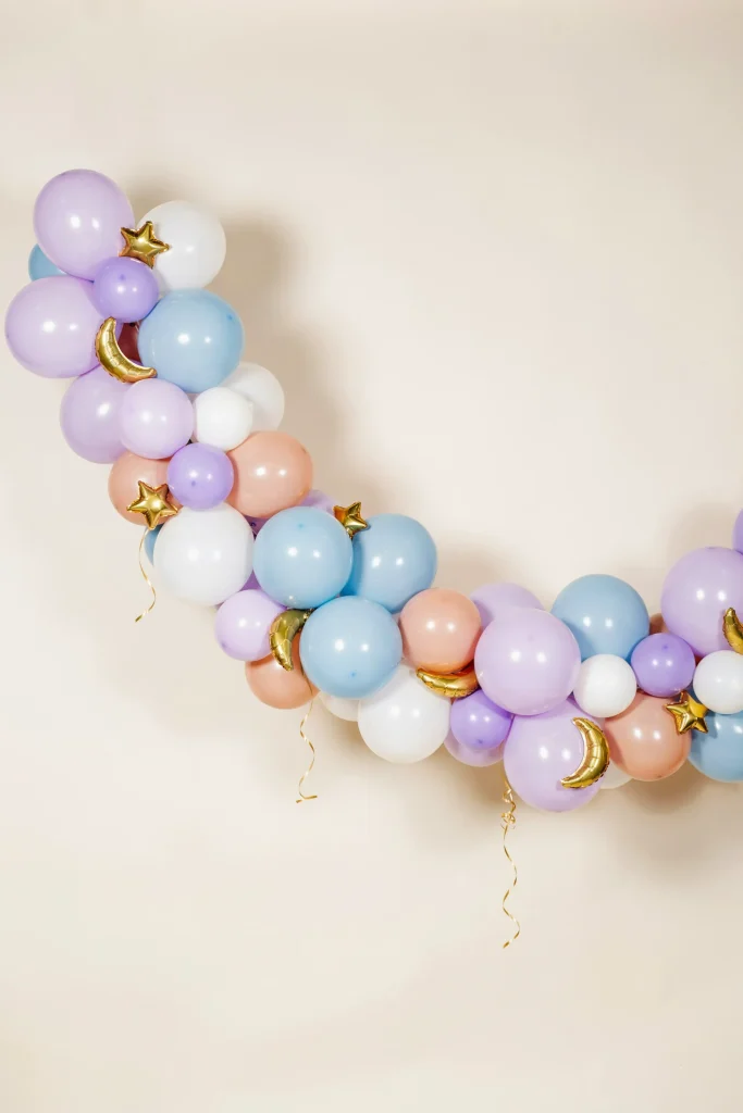 An organic balloon garland in lavender, soft blue, blush, and white, with a few metallic gold star and moon balloon accents woven throughout.