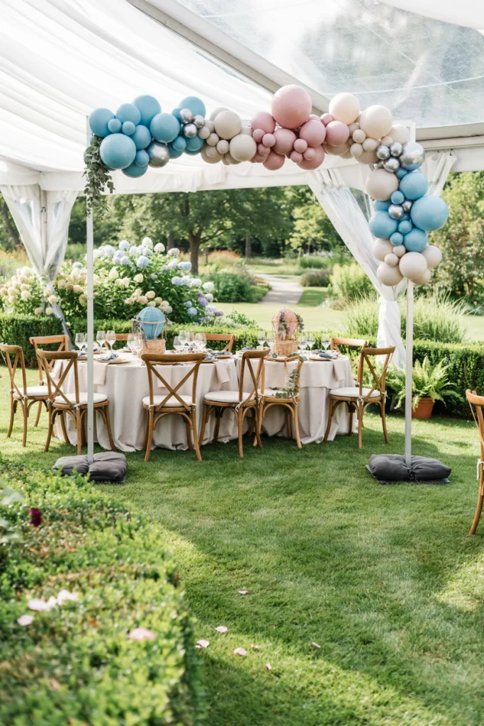 Outdoor garden hot air balloon baby shower setup with a balloon arch and round tables