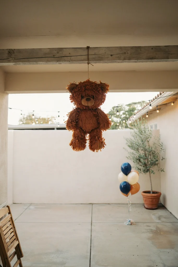 Bear-shaped piñata covered in layered cocoa-brown tissue paper fringe above navy balloons