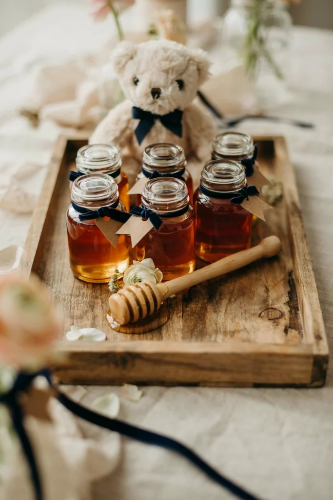 Small honey jar favors with kraft paper labels and navy ribbon on a wooden tray