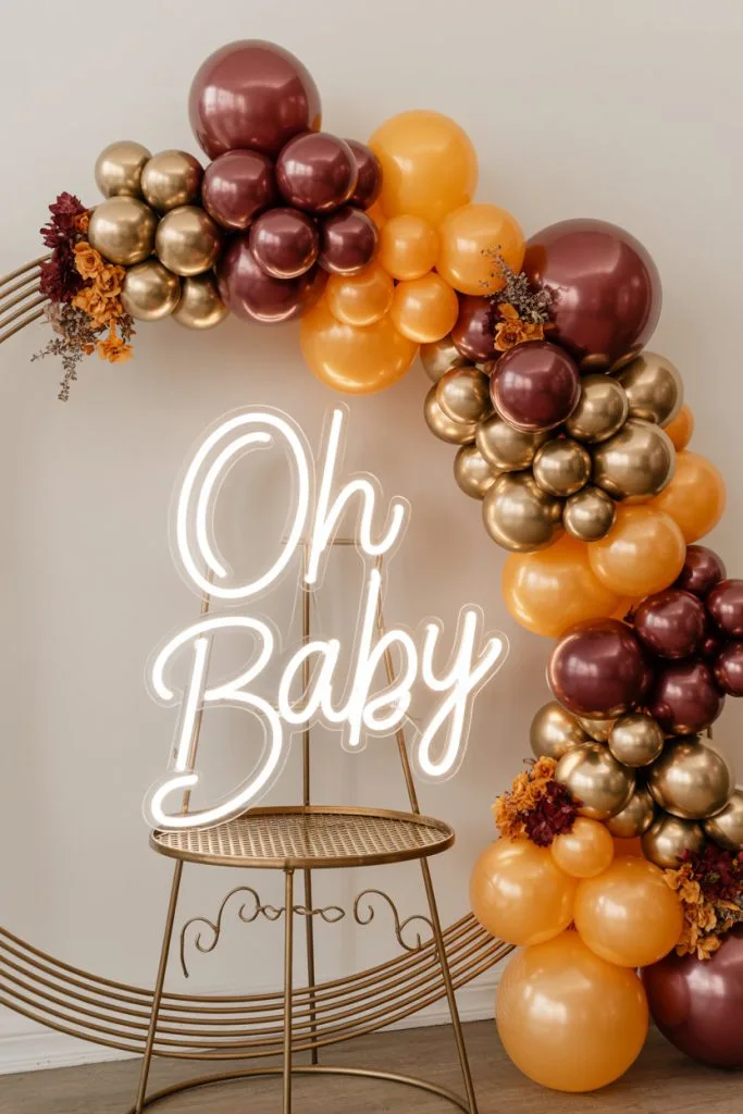 Glowing neon Oh Baby sign with burgundy and gold balloon garland
