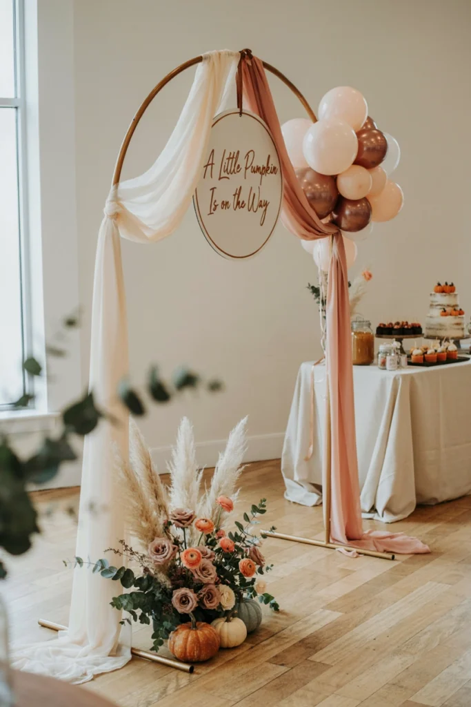 Metal arch stand draped in sheer fabric with pumpkin accents at the base
