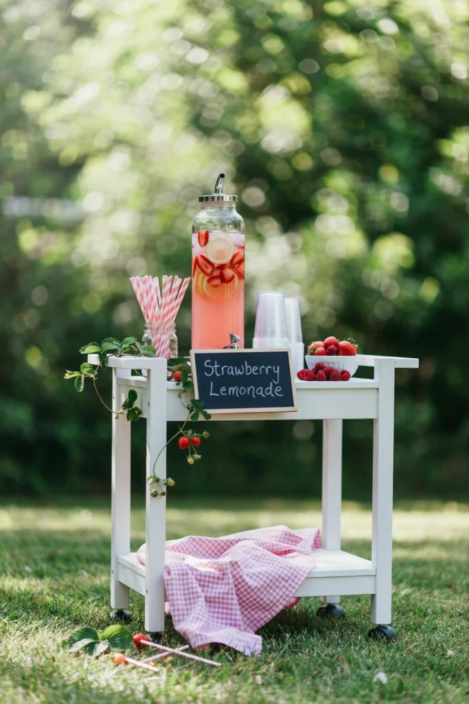 Drink cart with a glass dispenser of strawberry lemonade and stacked cups