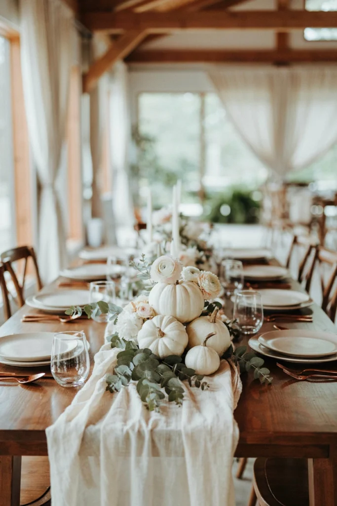A low centerpiece of white pumpkins nestled into a bed of eucalyptus and white ranunculus