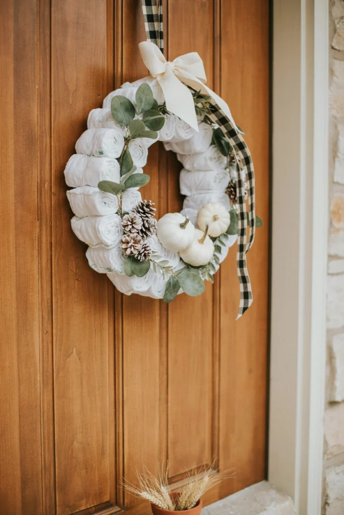 A wreath made entirely of rolled diapers wrapped in buffalo plaid ribbon, hung on the front door