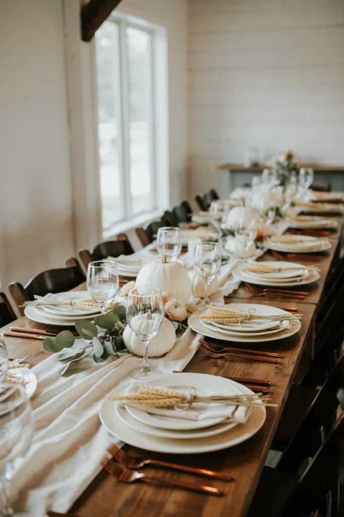 An all-ivory table setting with a few loose wheat stalks laid across each place setting instead of a floral centerpiece