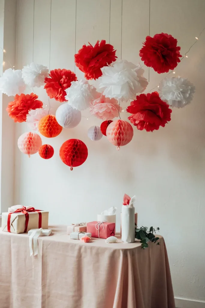 Red, pink, and white tissue pom poms and honeycomb balls hung above a baby shower gift table